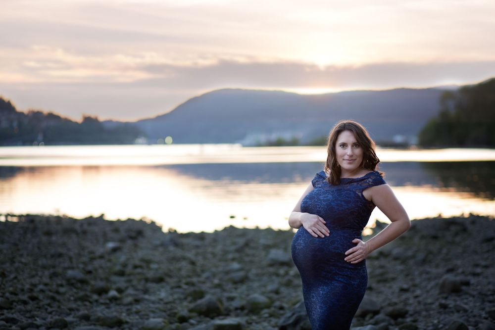 First time mom in a lace maternity gown poses in front of a beautiful sunset.