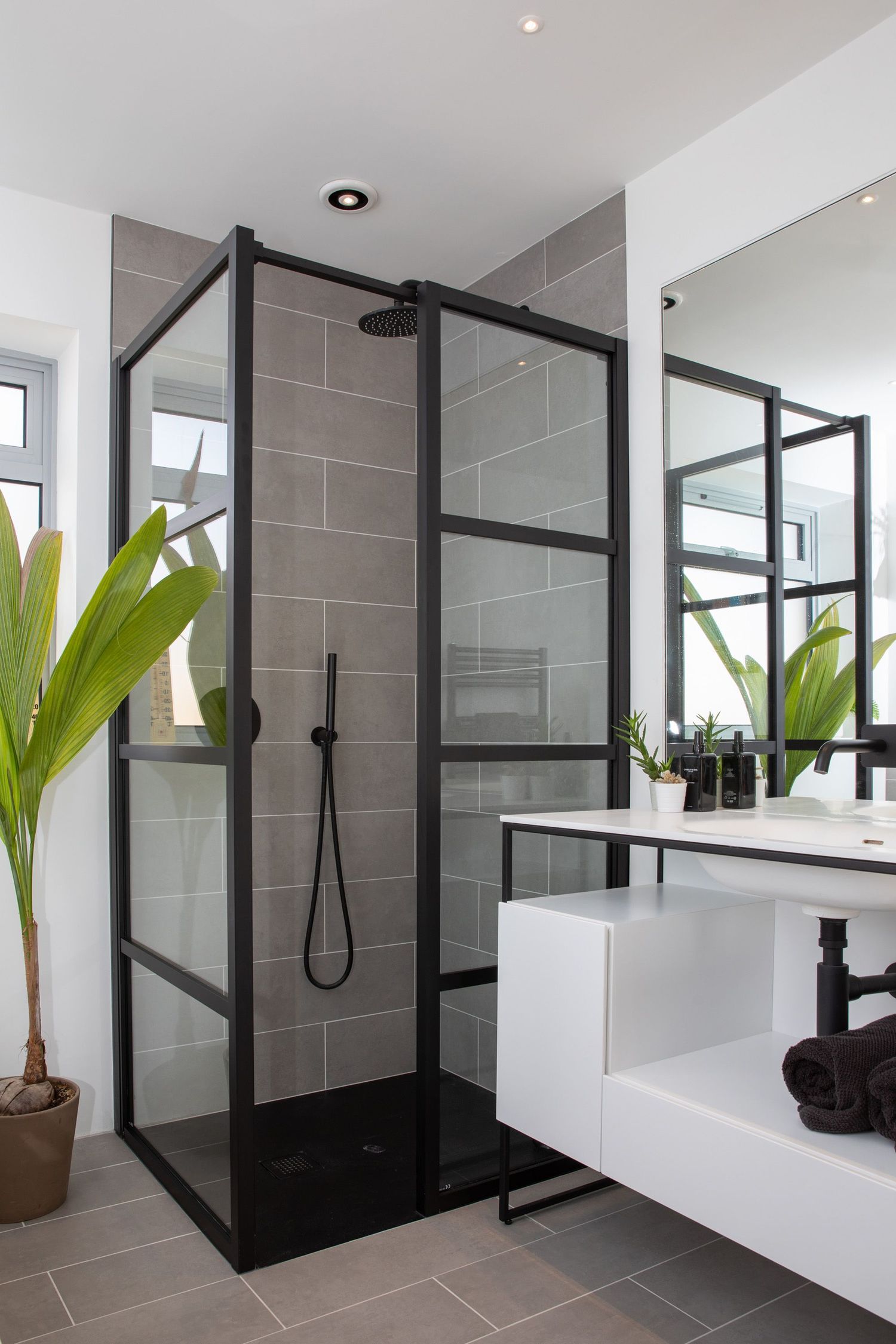 Contemporary bathroom with black-framed glass shower enclosure and gray tile walls.