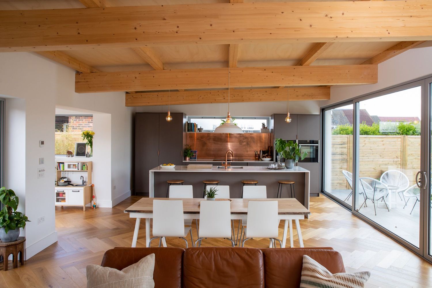 Open concept kitchen and dining area with wooden beam ceiling and large windows.