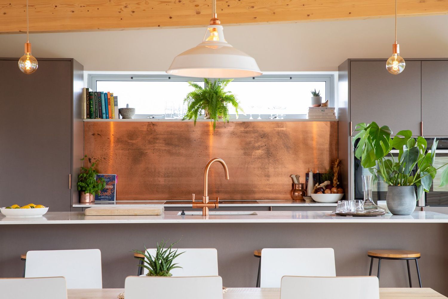 Modern kitchen with copper backsplash, pendant lights, and white dining chairs.