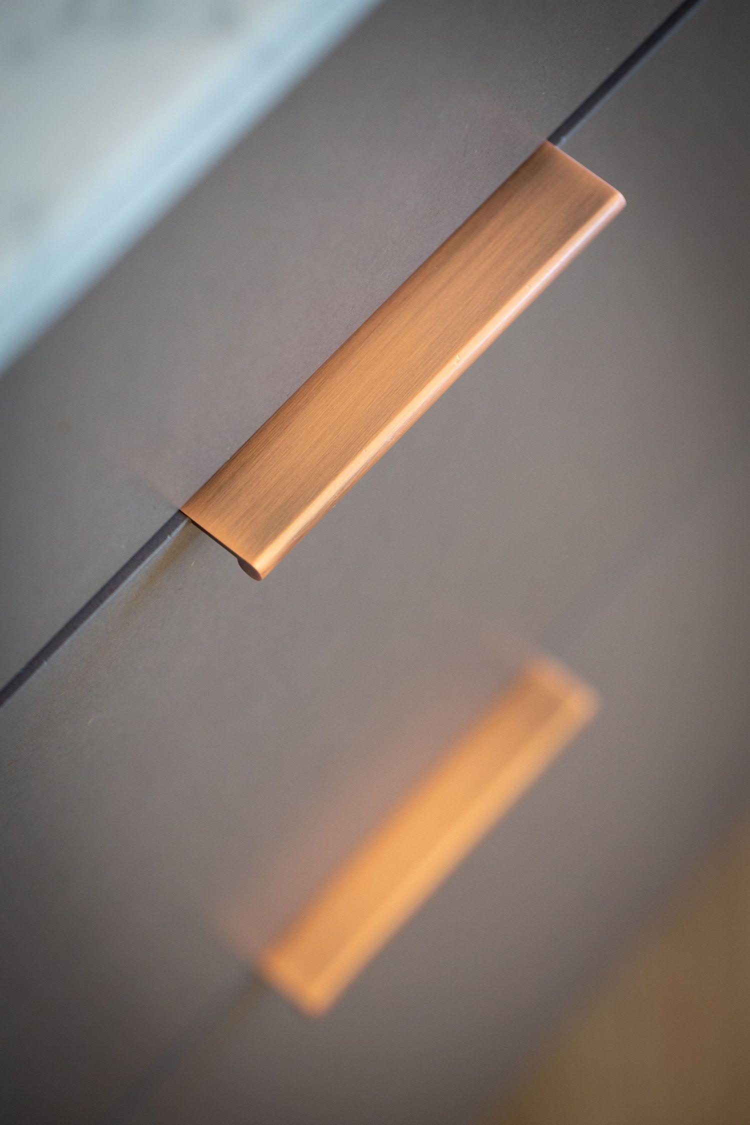 Close-up of minimalist copper cabinet handle against gray surface.