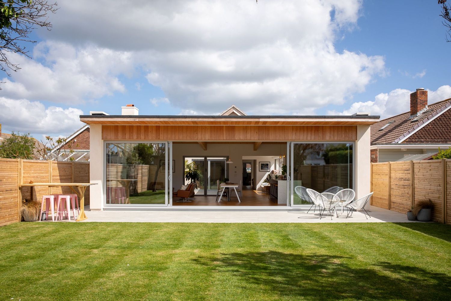 Modern garden room extension with full-width glass doors opening onto a manicured lawn with contemporary outdoor furniture.