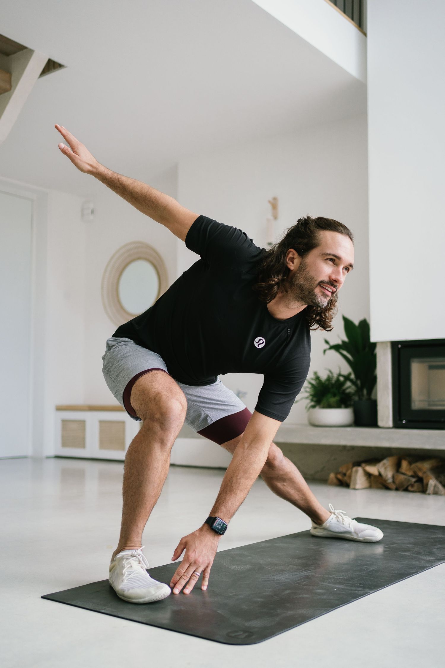 Person demonstrating a stretching exercise pose on a dark yoga mat indoors.