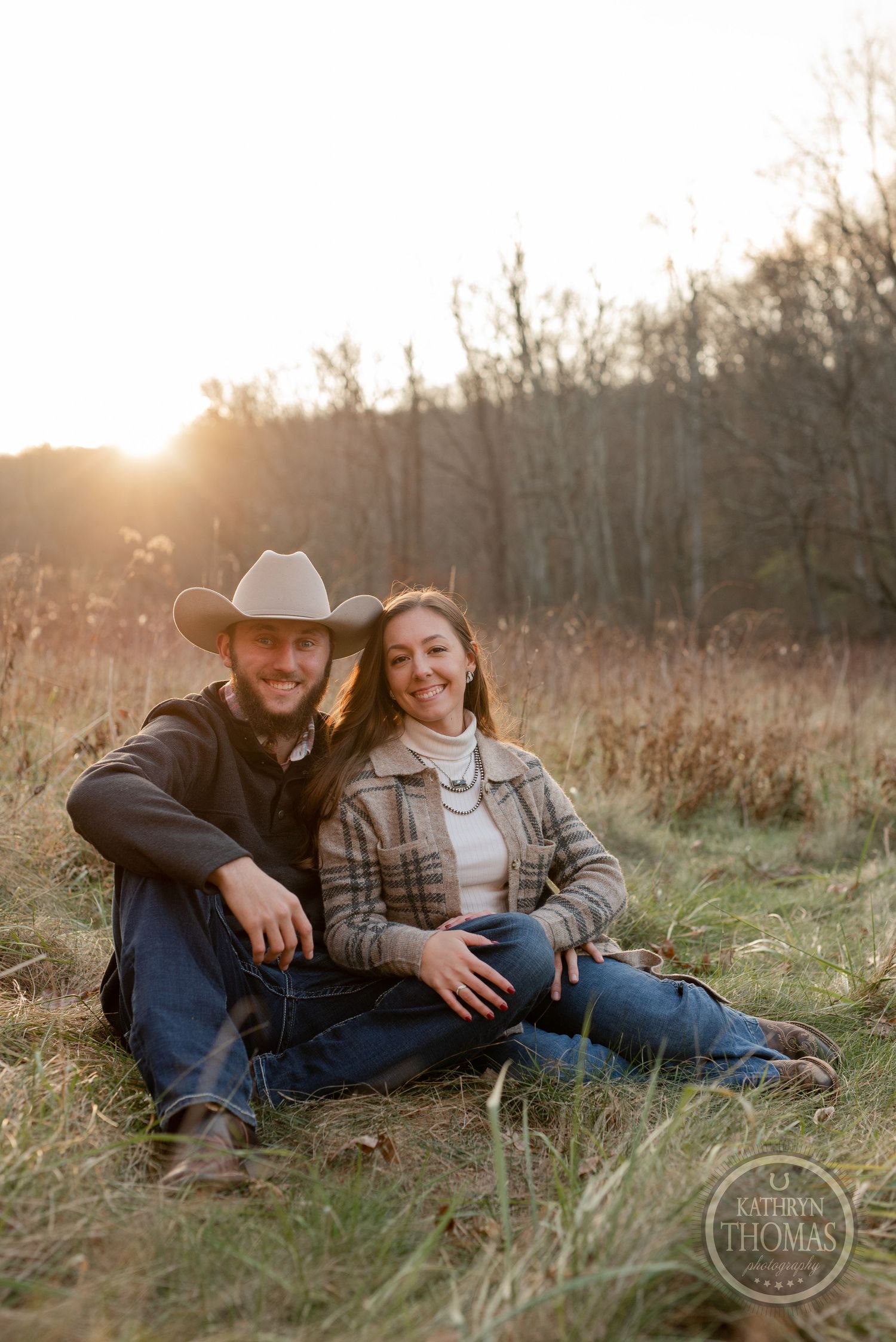 A couple in casual western wear poses together in a golden meadow at dusk.