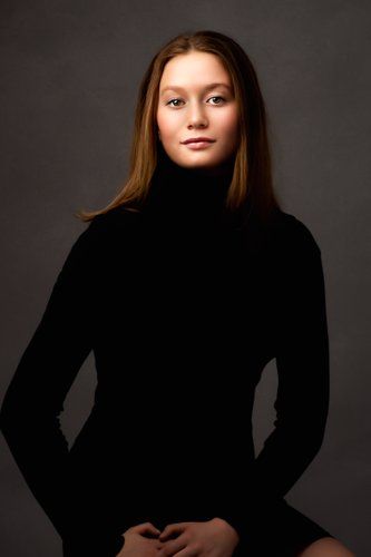 Studio portrait of a young person in a black turtleneck sweater against a dark background.