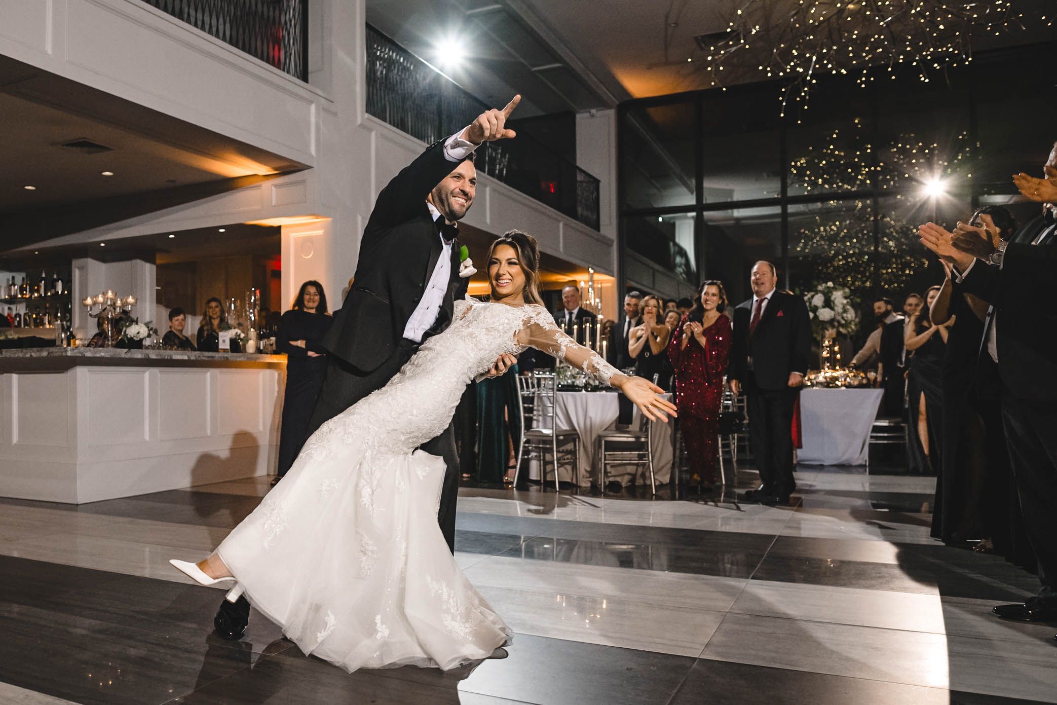 Wedding couple shares their first dance surrounded by guests in an elegant indoor reception venue.