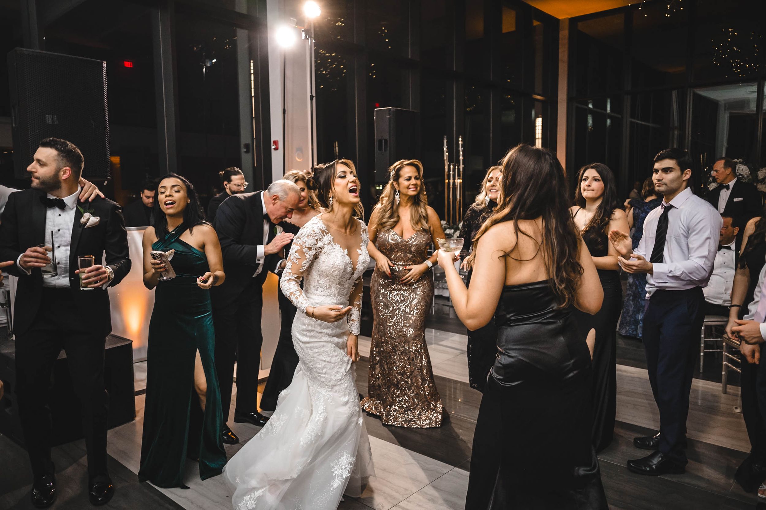 Wedding reception venue with guests mingling and dancing under ambient lighting.