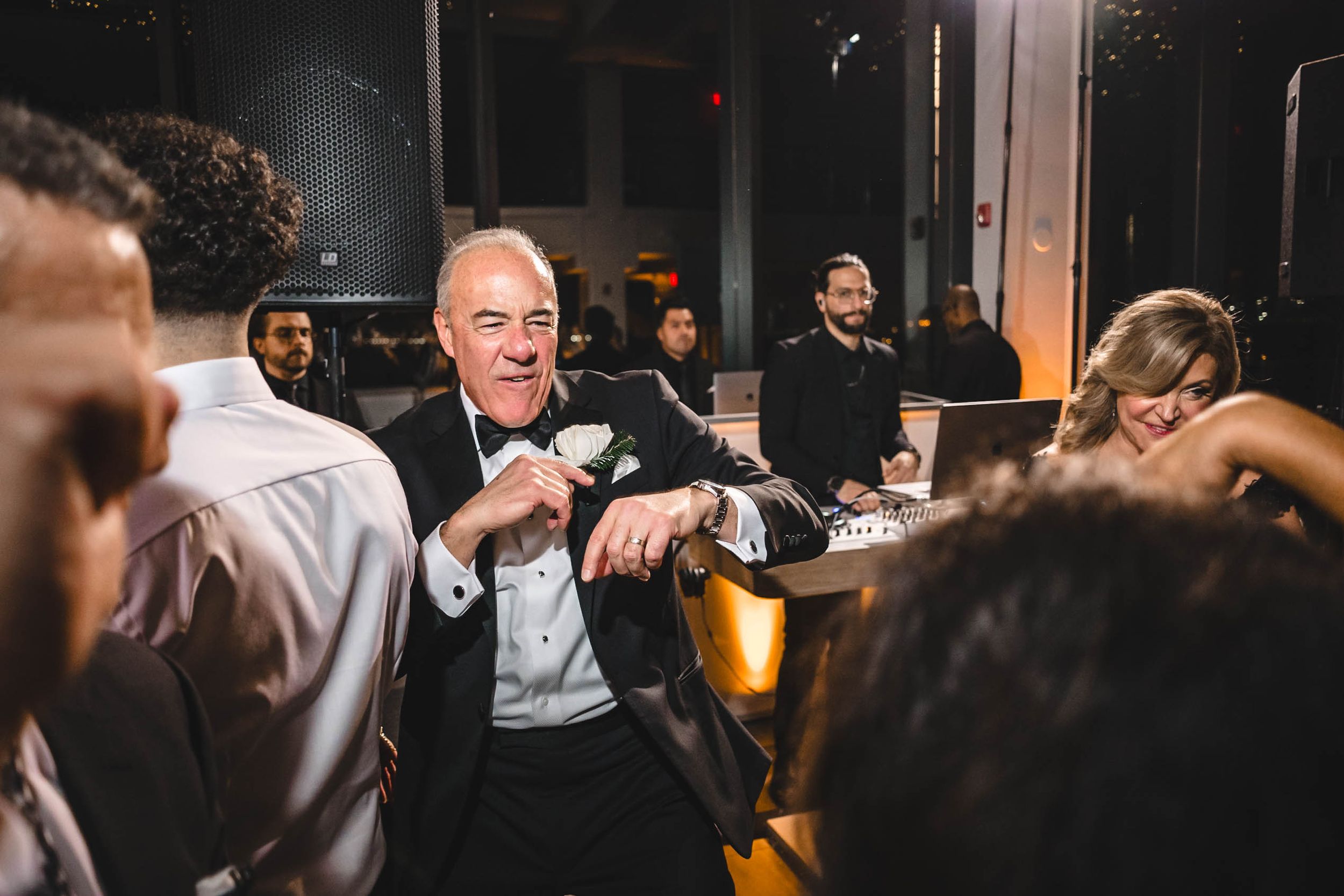 Wedding reception crowd dancing and celebrating in a dimly lit venue space.