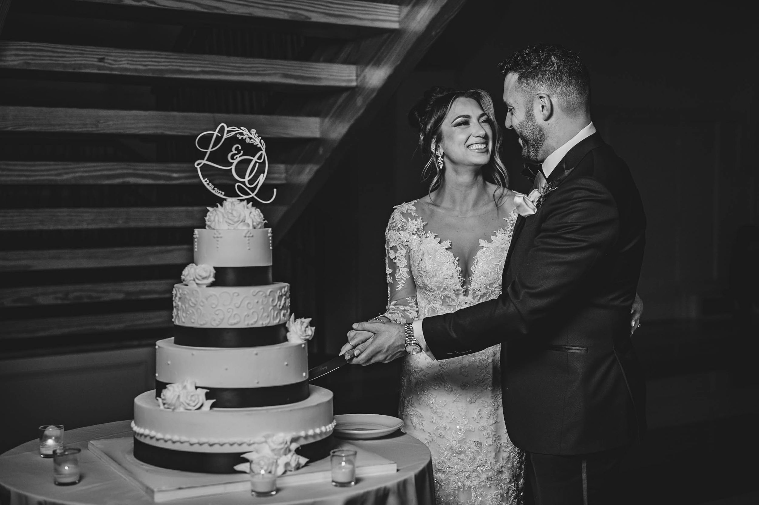 Black and white photo of wedding cake cutting moment at an elegant reception.