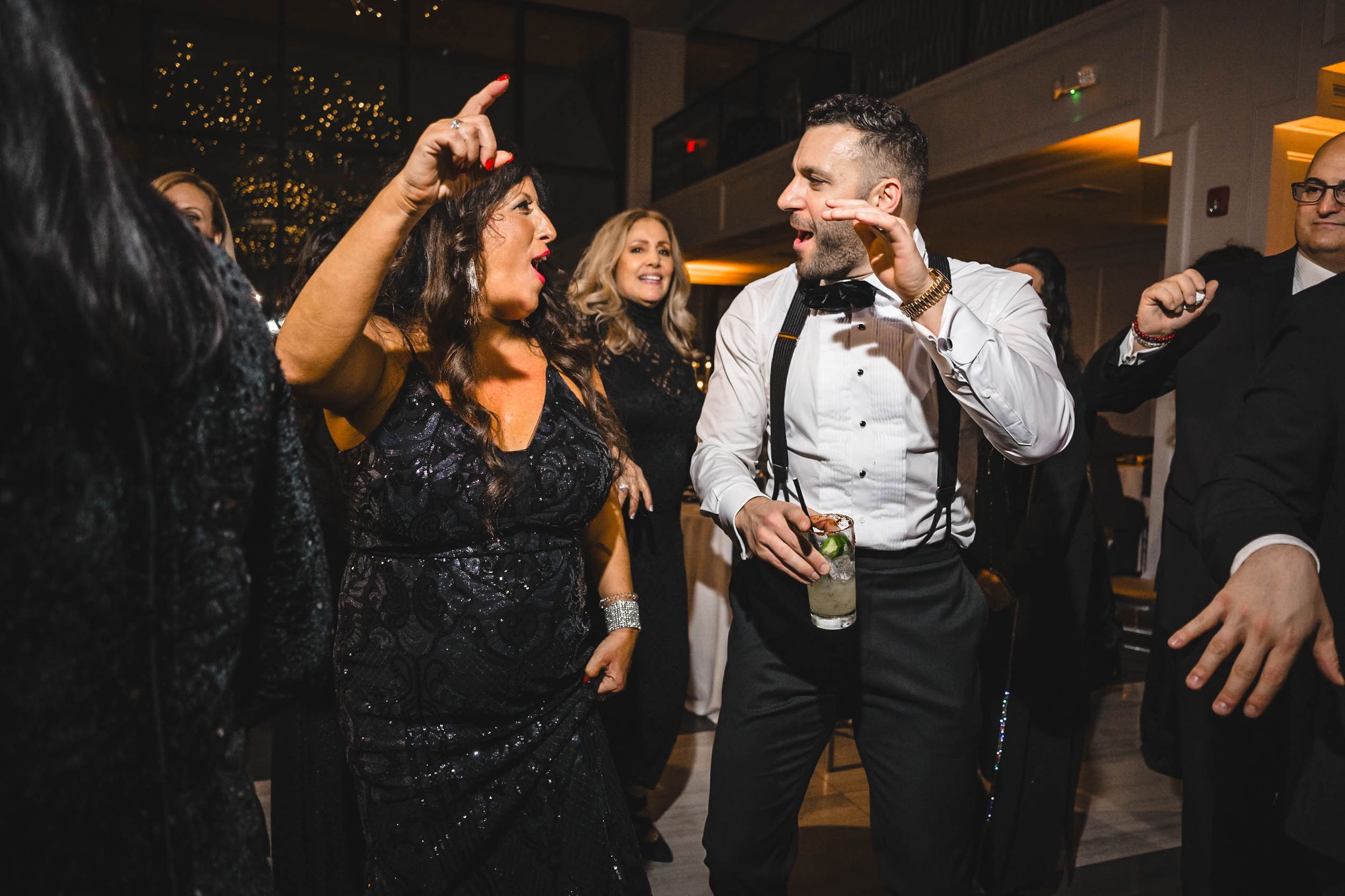Wedding party dancing and celebrating in a dimly lit reception venue.