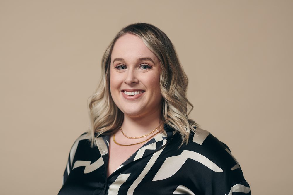A professional headshot portrait against a neutral beige background.