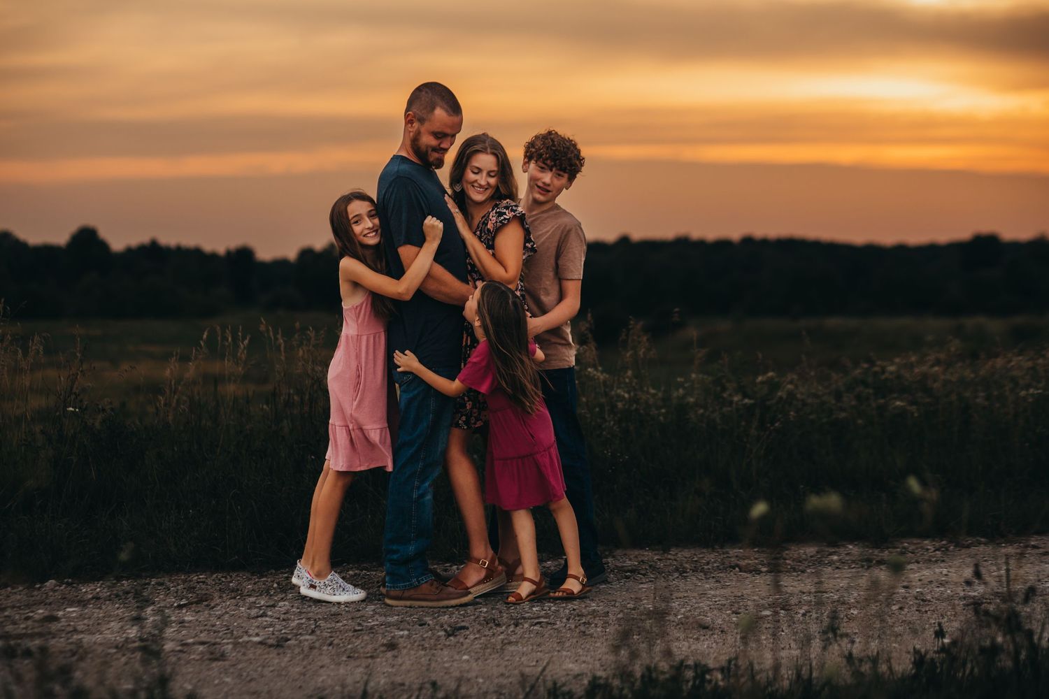 Family of four posing together against dramatic sunset sky during outdoor session.