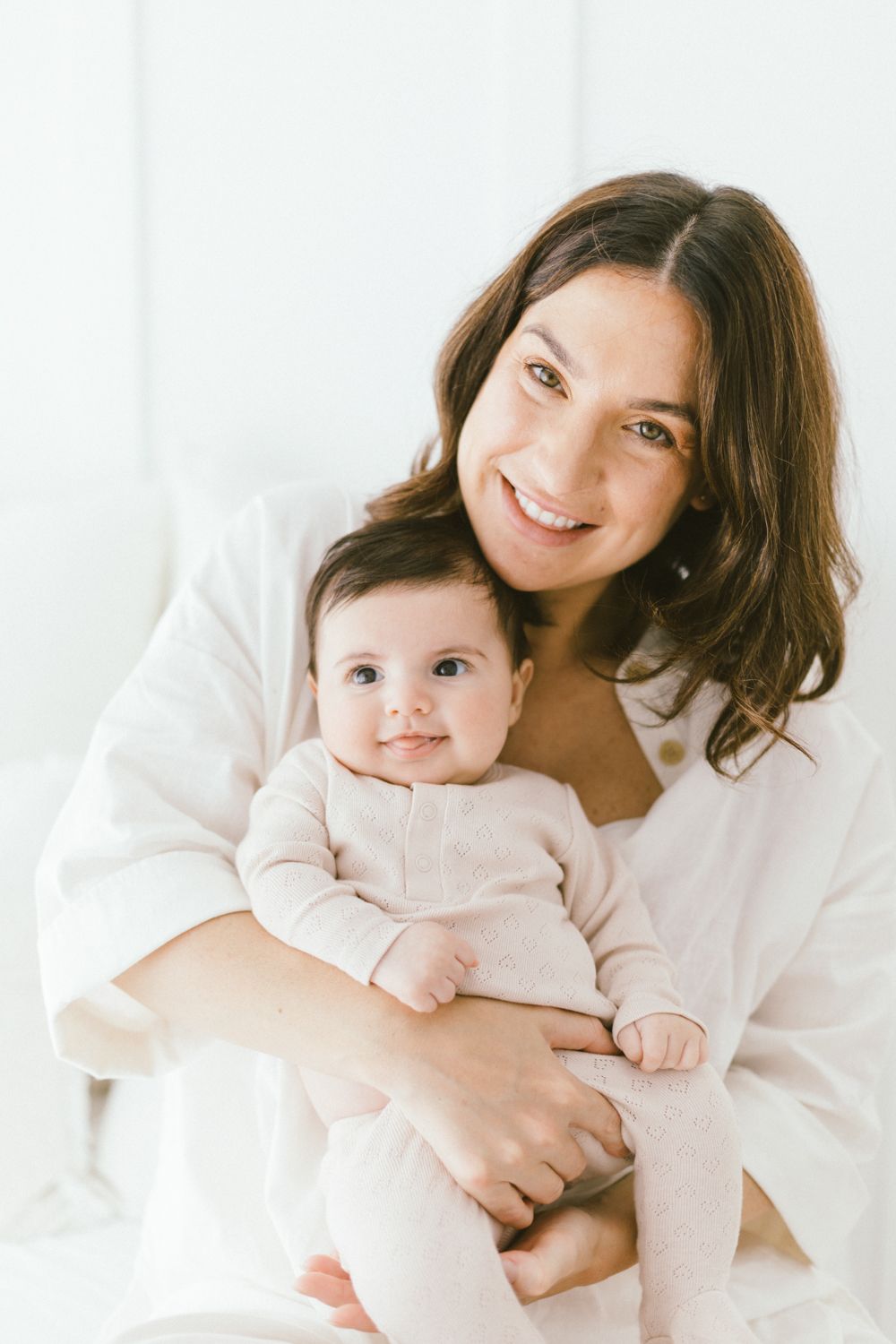 Joyful portrait of caregiver holding baby in matching white and beige outfits.