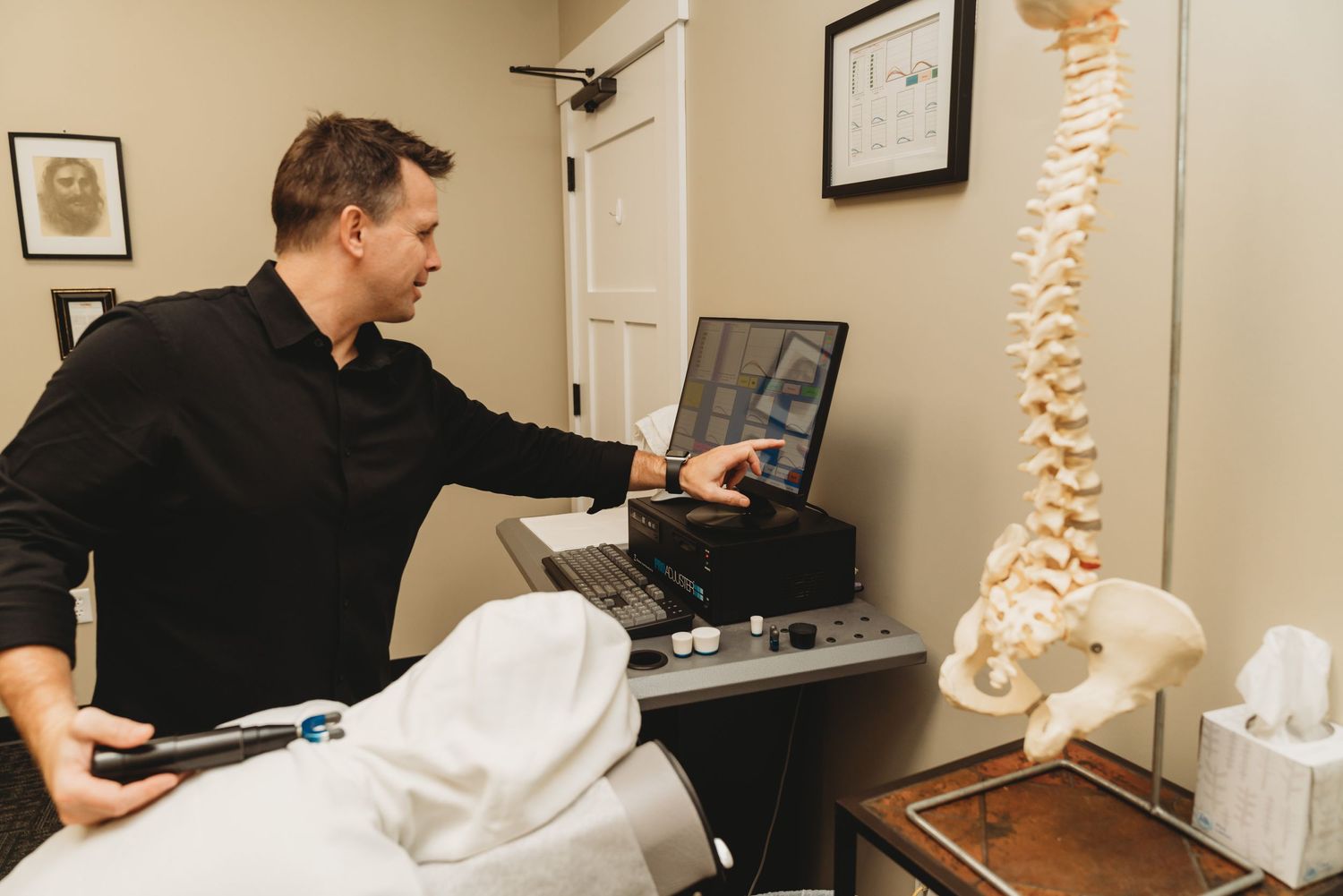 Healthcare provider adjusting medical equipment near spine model in examination room.
