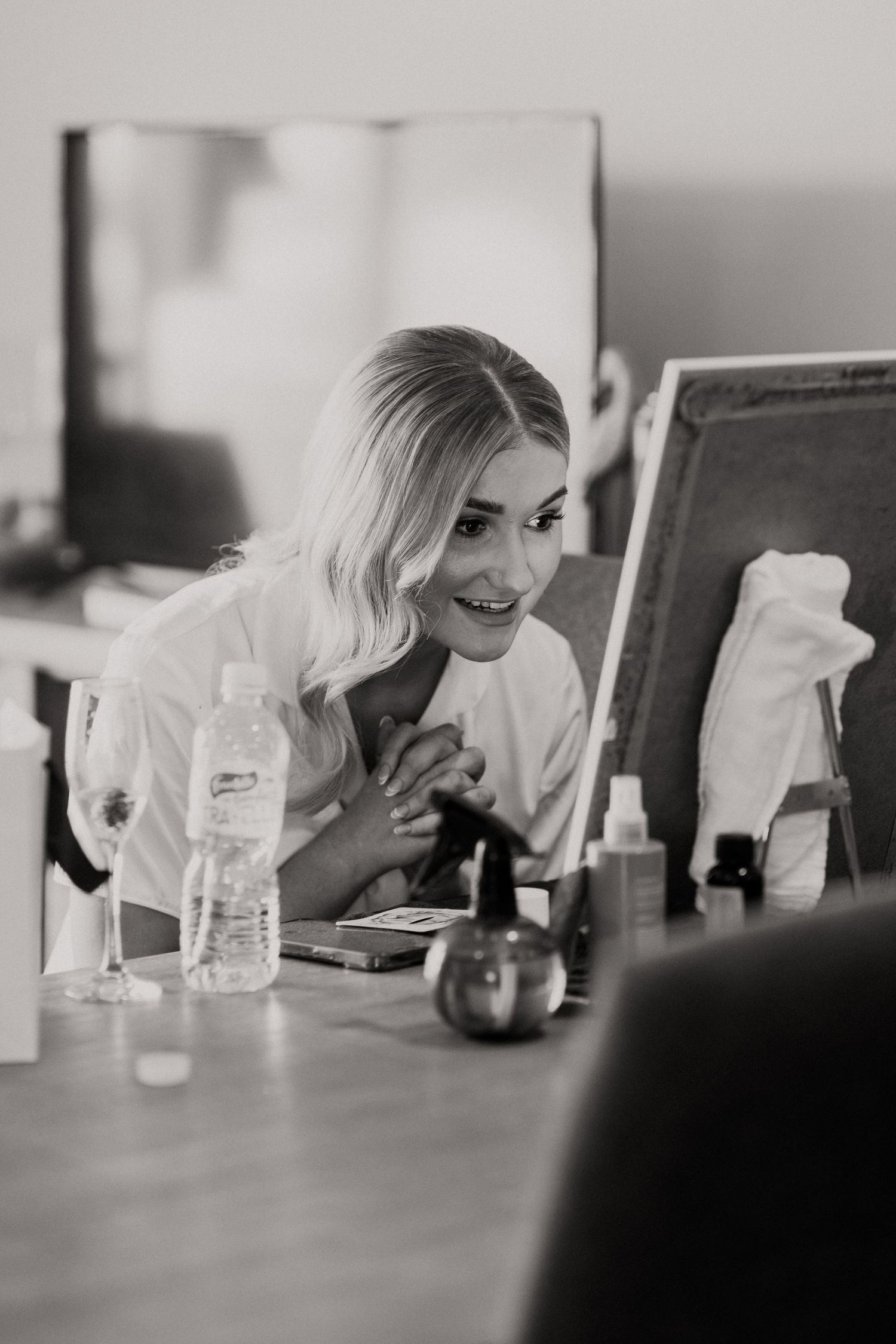 A smiling figure leans over a desk with beauty products and a mirror.