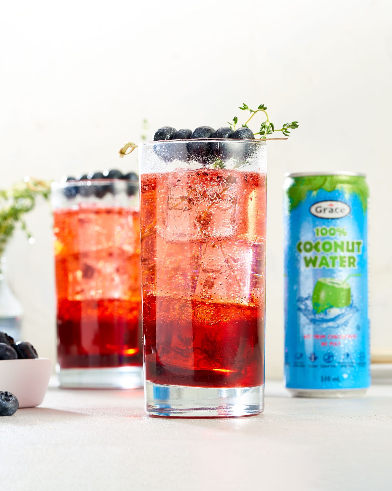 Colorful tropical cocktails with fresh berries and coconut water displayed in glasses on white marble counter.
