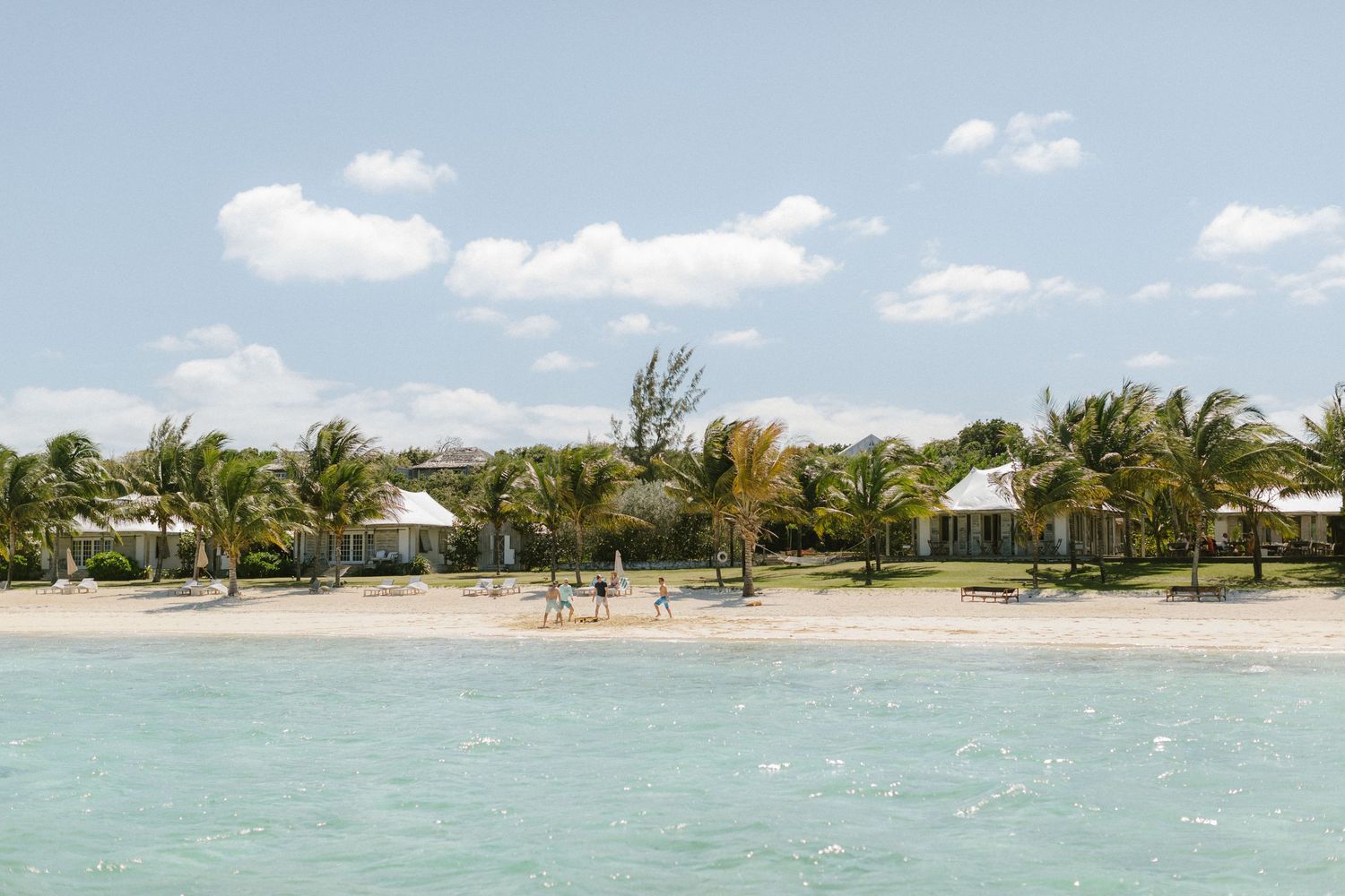 Beachfront resort cottages with palm trees line the shore of crystal clear turquoise waters on a tropical paradise.