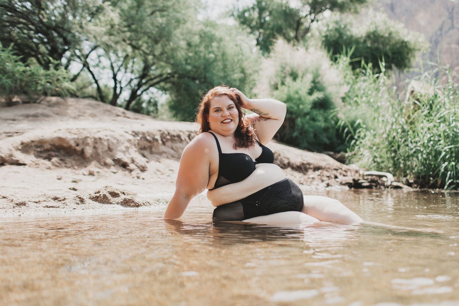 Body positive portrait of woman in black swimwear relaxing in shallow natural water.