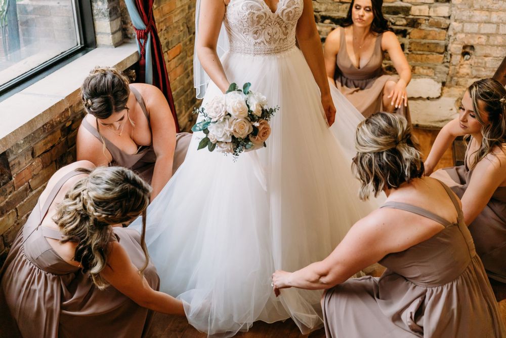 Bridesmaids in mauve dresses helping adjust the bride's gown before the ceremony.