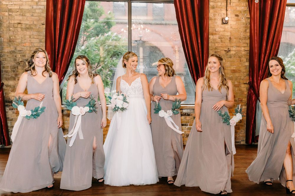 Wedding party lined up in mauve bridesmaid dresses and white bridal gown against brick wall.