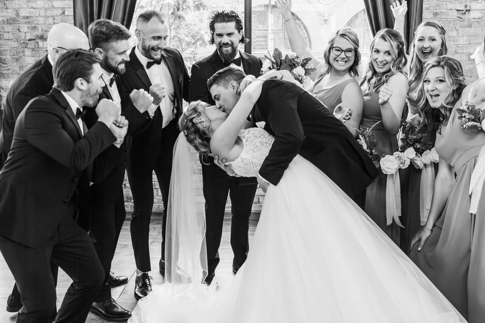 Wedding party celebrating with excitement in front of exposed brick wall.