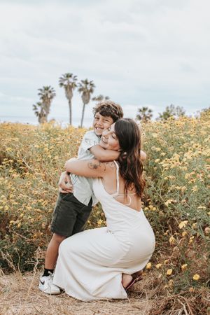 A joyful embrace shared in a field of yellow wildflowers with palm trees behind.
