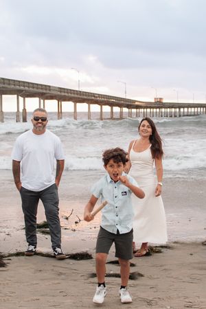 Beach photoshoot with family members playing near ocean pier during overcast day.
