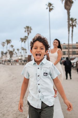 Joyful child laughing and playing on beach with palm trees and buildings in background.