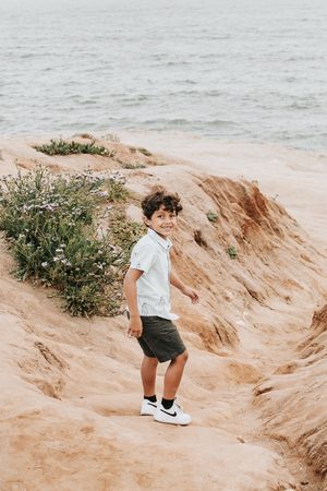 Young child running and playing on sandy cliffs near the ocean during daytime.