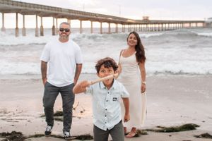 Family playing and posing near oceanside pier during cloudy beach day.
