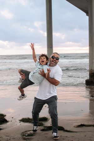 Joyful dance moves captured under beach pier during sunset.