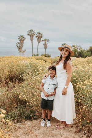 Mother and child stand together in a field of wildflowers with palm trees in distance.