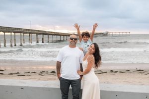 Family enjoying playful moments together on a cloudy beach with pier in background.
