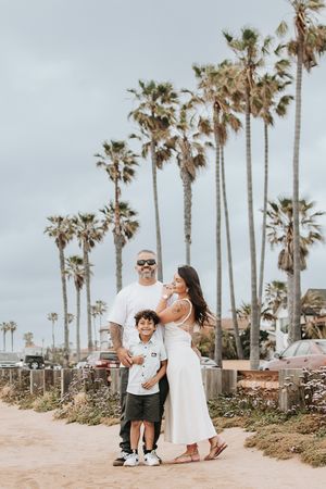 Family standing together on beach path with iconic California palm trees in background.