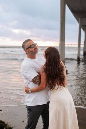 Romantic sunset beach photoshoot showing playful interaction under a pier.
