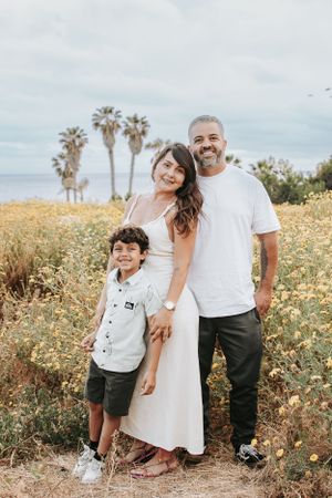 A family poses together on a coastal path with palm trees and yellow wildflowers.