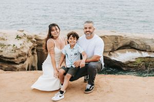 Family enjoying a casual day at a rocky coastal beach area with palm trees in the background.