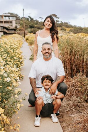 Family portrait on coastal path surrounded by yellow wildflowers and palm trees.