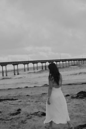 Black and white beach scene with long wooden pier extending into the ocean.