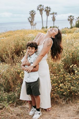 Joyful embrace shared in a coastal field of yellow wildflowers with palm trees and ocean views.