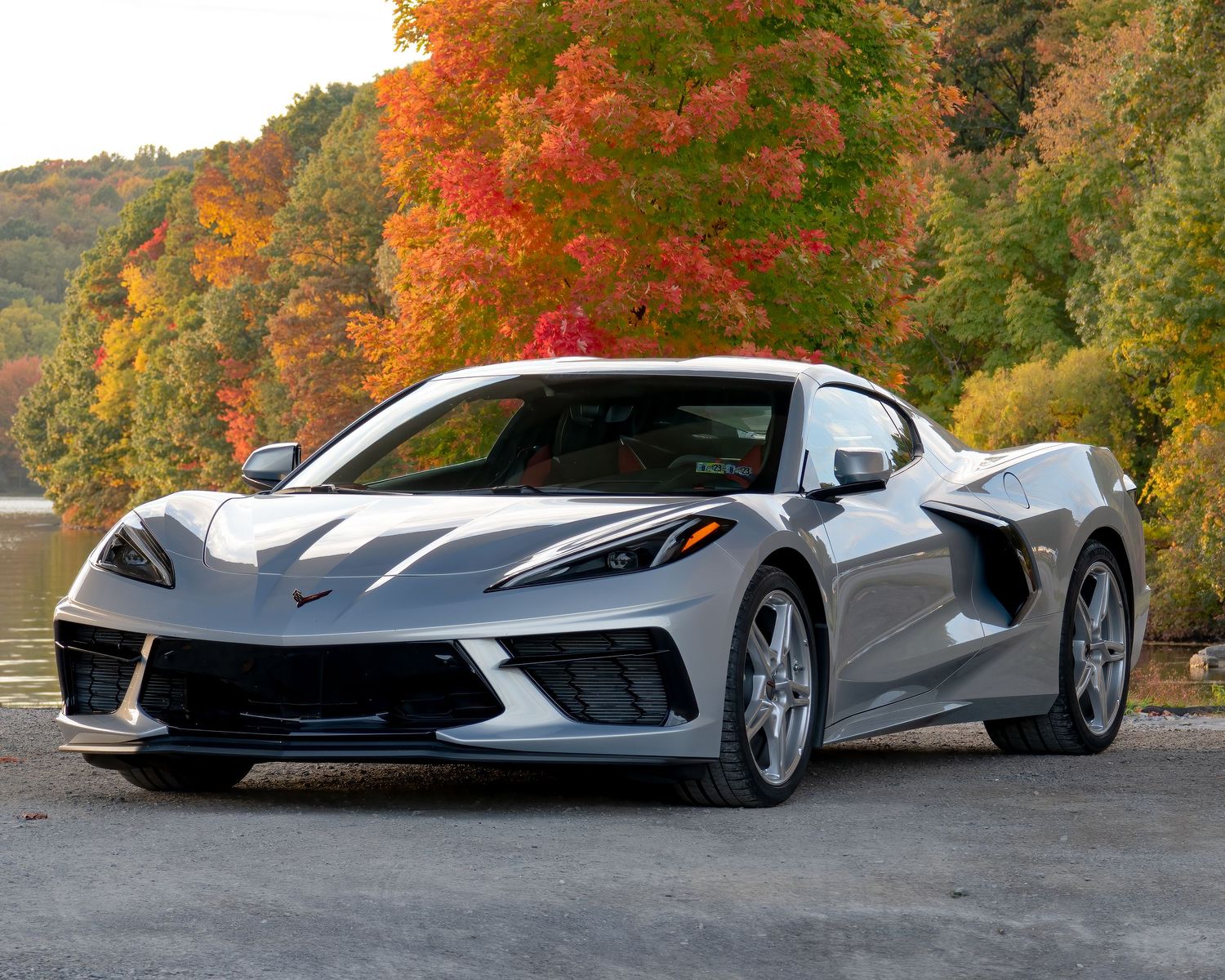 A silver Chevrolet Corvette C8 parked against a backdrop of vibrant autumn foliage.