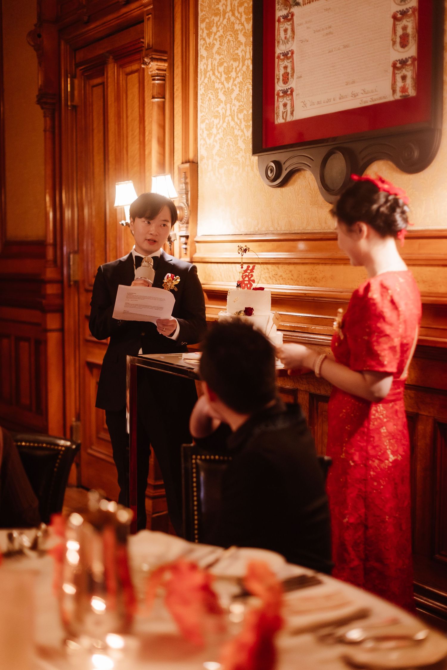 Wedding reception scene in an ornate wooden-paneled room with red traditional dress.