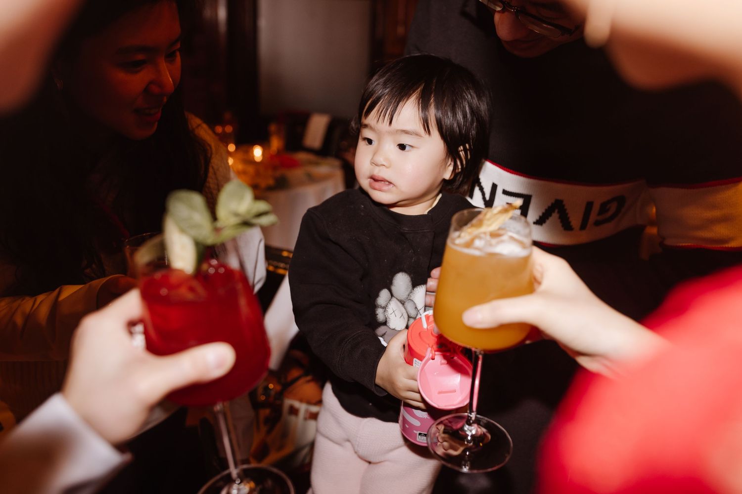 Young child watches adults toast with colorful cocktails during celebration.