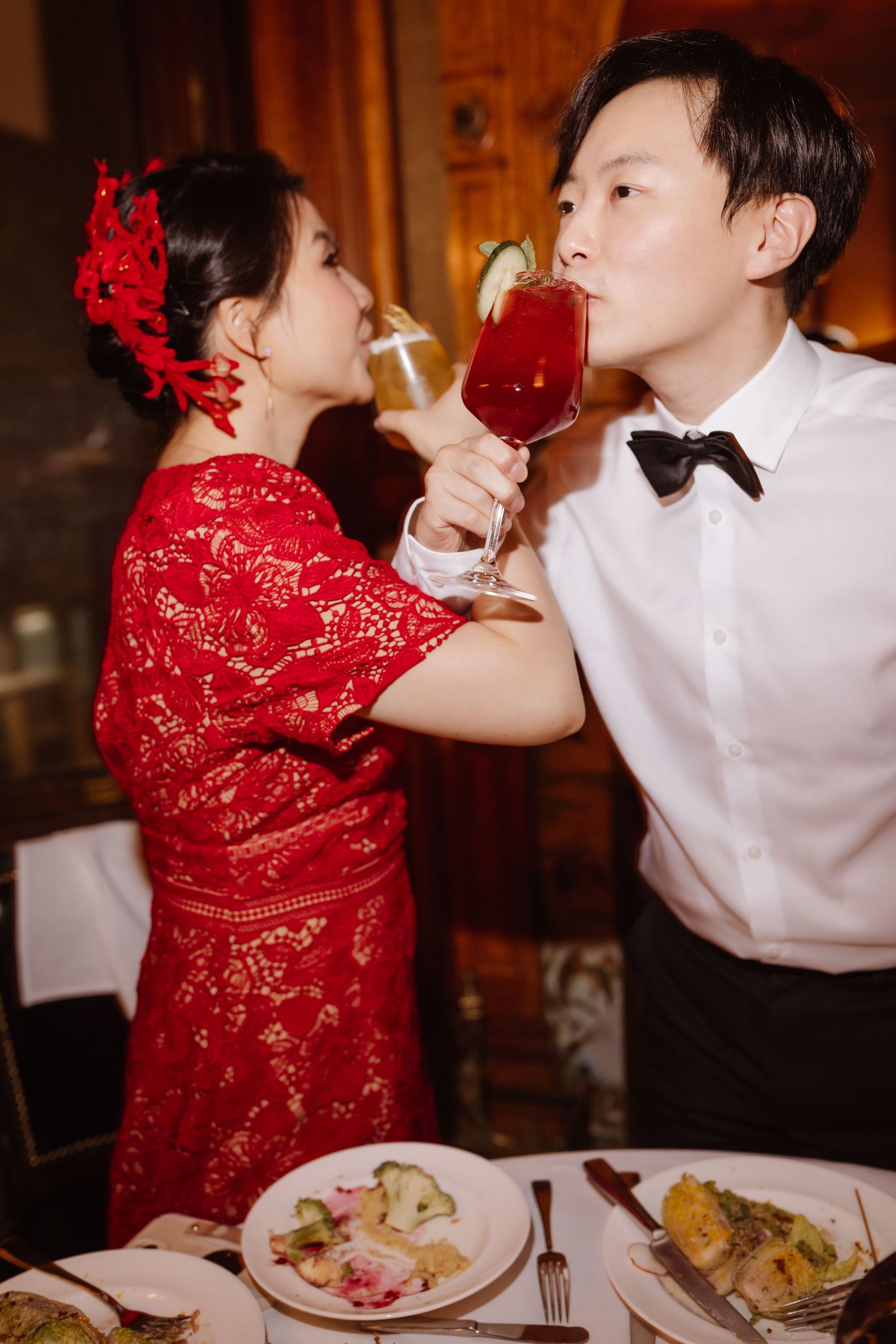 Couple in formal wear sharing drinks at reception dinner with red traditional dress.
