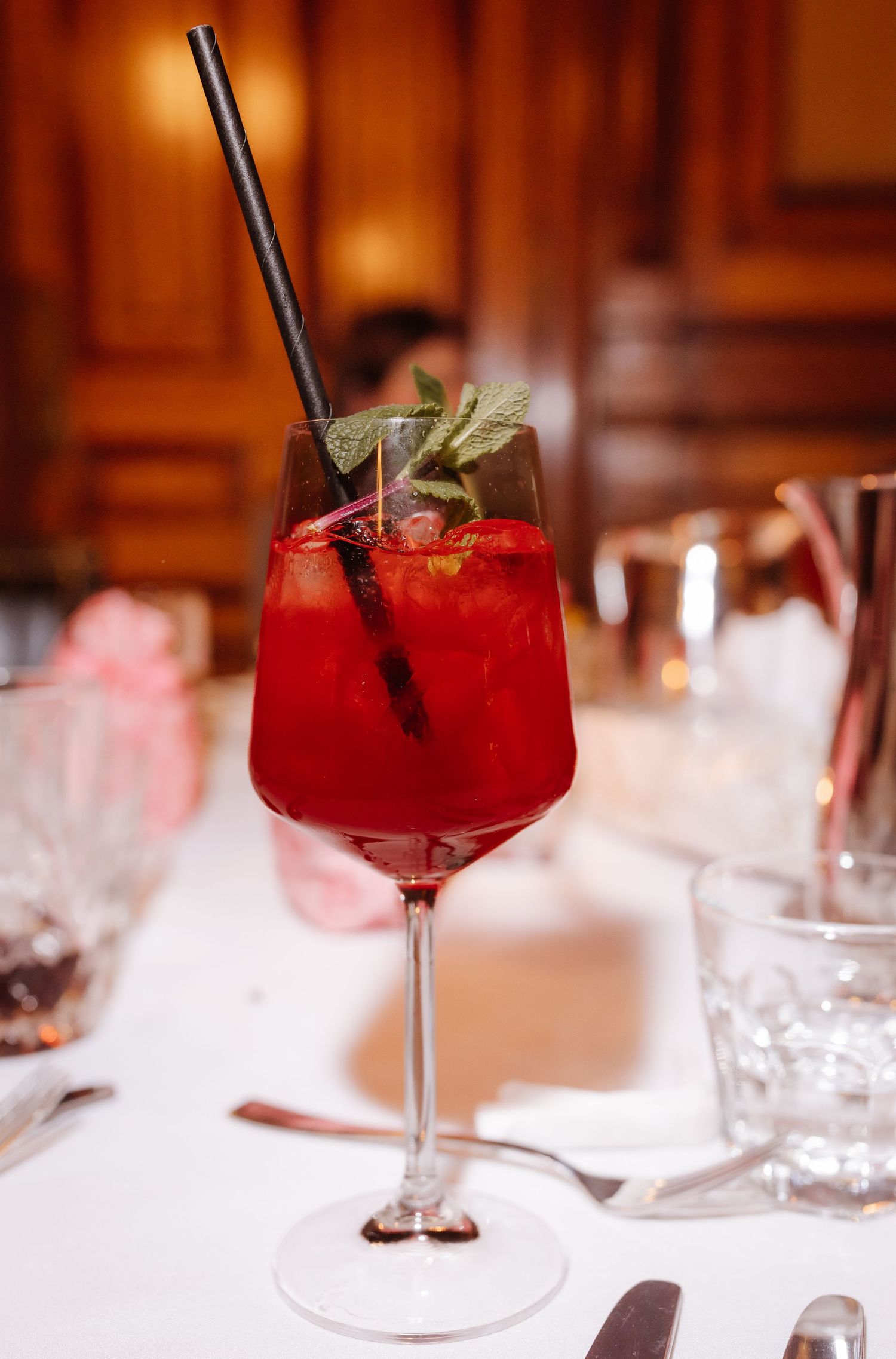 Red cocktail garnished with mint leaves in stemmed glass on white tablecloth.