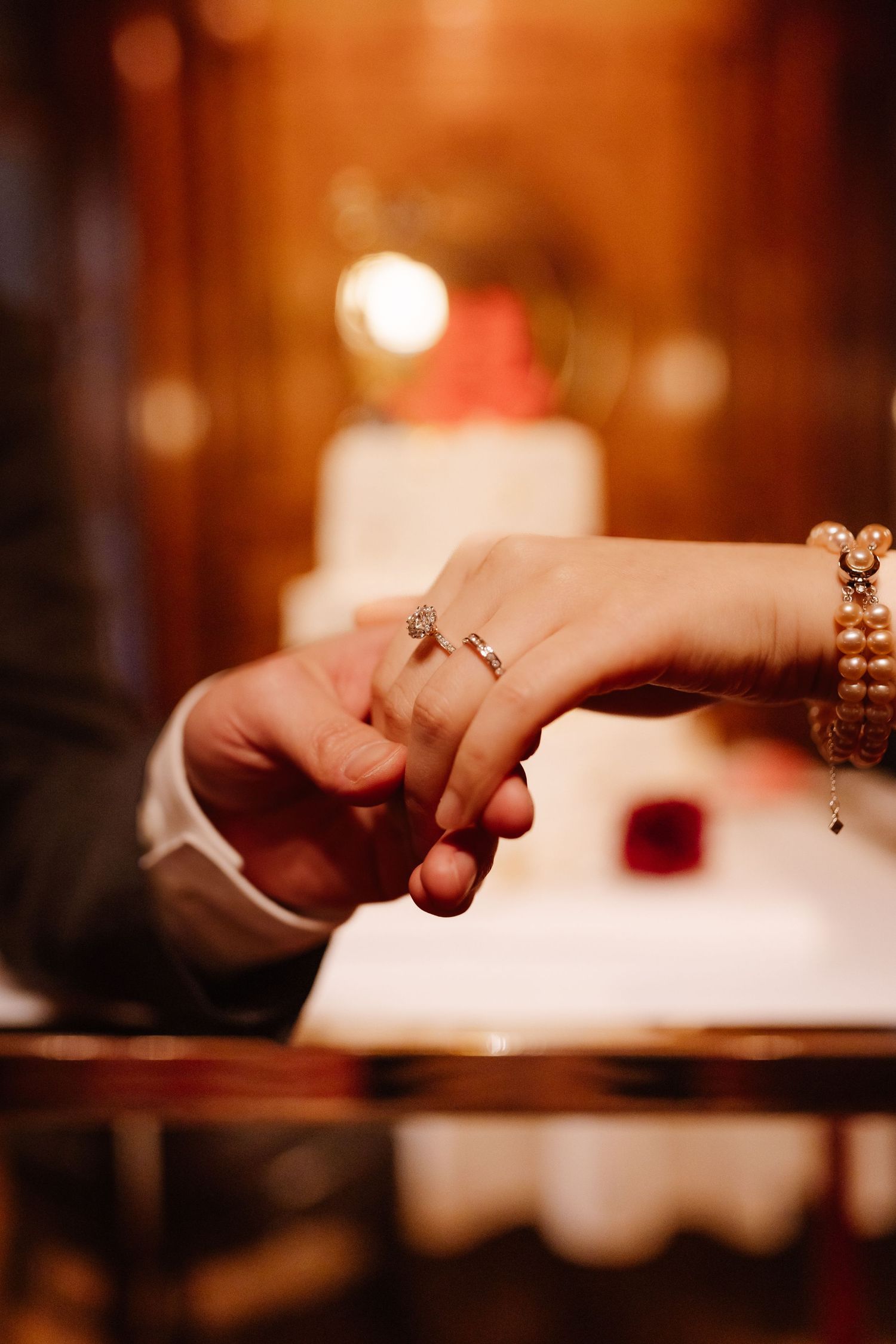Close-up shot of hands with engagement ring in warm lighting at an elegant dinner setting.