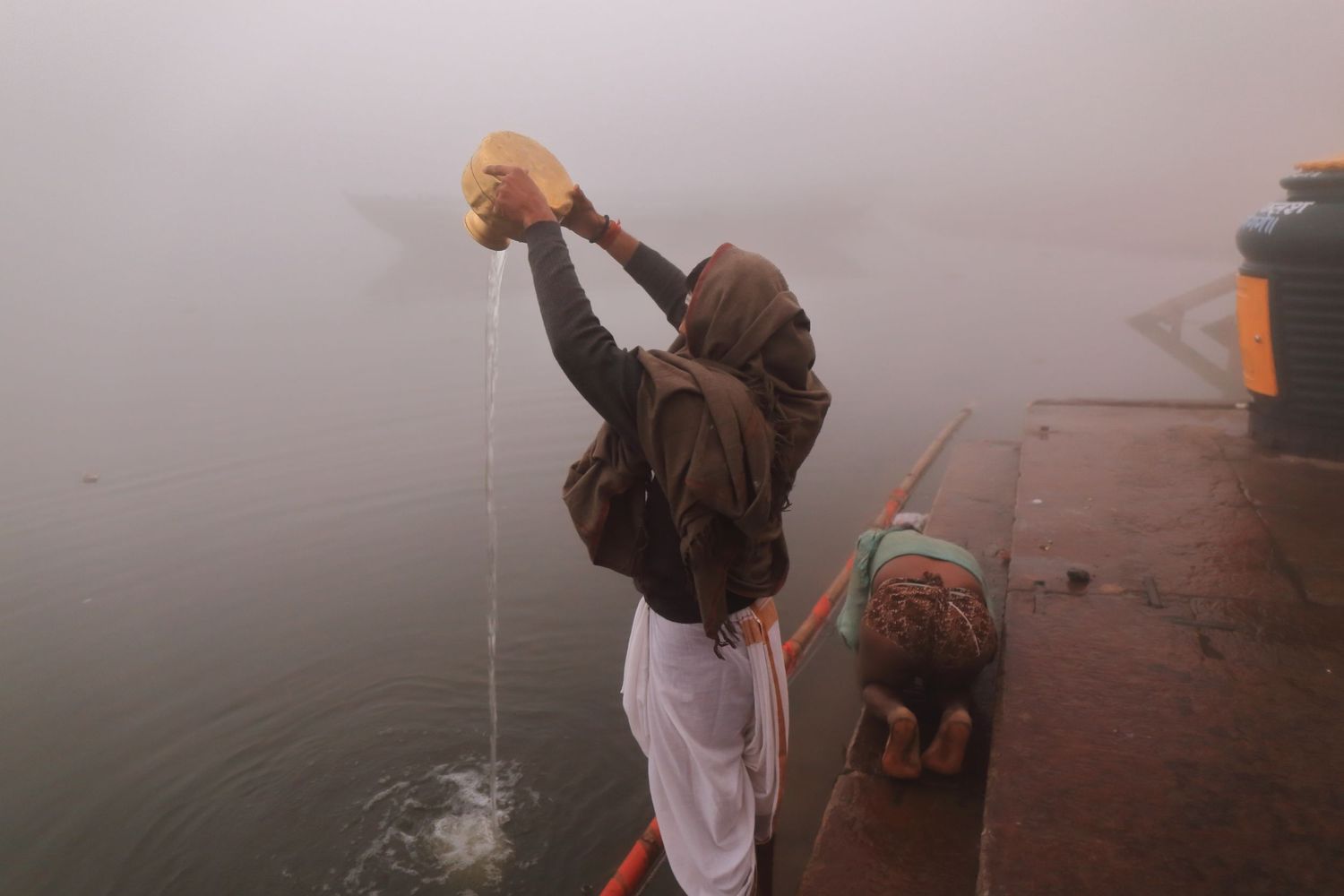 Devotee performing morning ritual offering at misty Varanasi ghat.