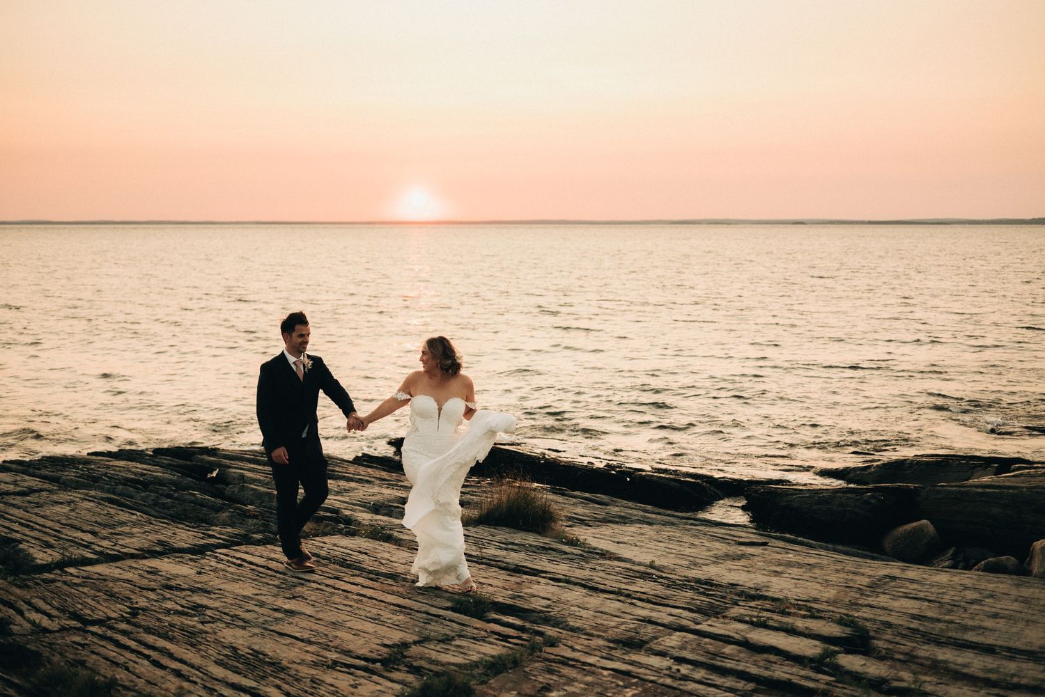 Couple dancing on rocky shore during golden sunset over ocean.
