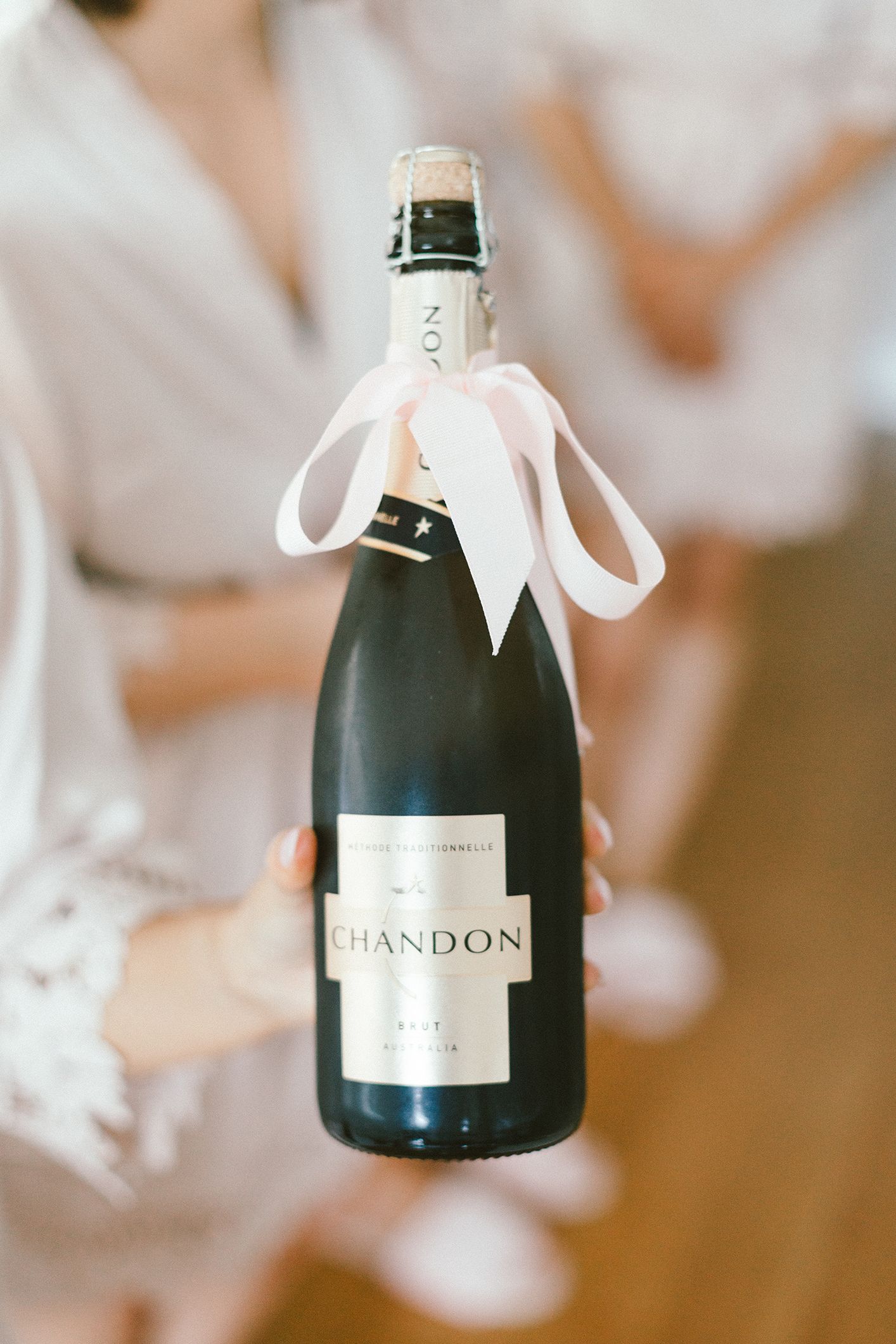 Champagne bottle with white ribbon bow and Chandon label on dark glass.