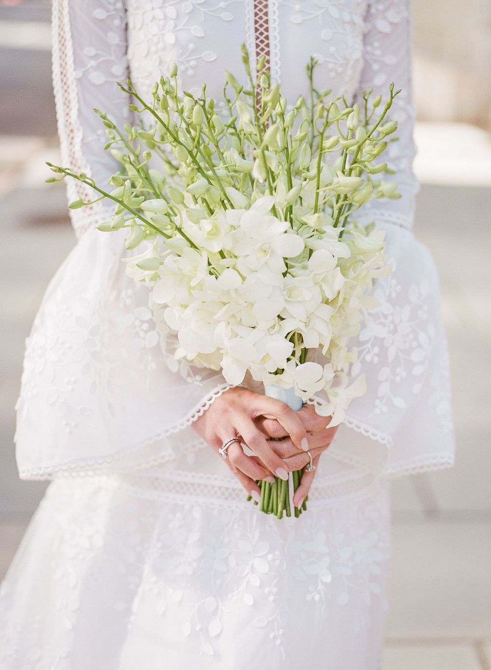 Elegant white floral wedding bouquet with delicate greenery held against a lace dress.